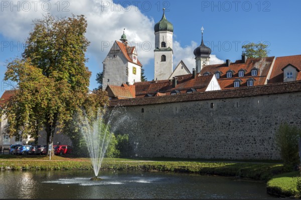 Trench pond with water fountain, city wall, church towers and water tower at the back, Isny, Allgäu, Baden-Württemberg, Germany