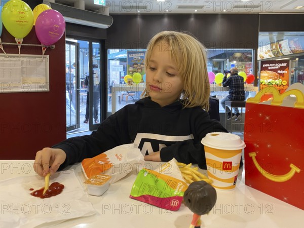 Interior view, child, boy, 7 years, blonde, eating Happy Meal, children's menu, at McDonald's restaurant, drink, French fries, ketchup, balloons, logo, Stuttgart, Baden-Württemberg, Germany
