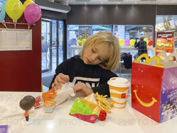 Interior view, child, boy, 7 years, blonde, eating Happy Meal, children's menu, at McDonald's restaurant, drink, French fries, balloons, logo, Stuttgart, Baden-Württemberg, Germany