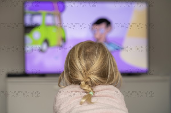 Child, girl, 4 years old, blonde, lying on sofa, watching TV, watching television, in front of television, from behind, braid, monitor, children's program, children's program, children's television, colorful, Stuttgart, Baden-Württemberg, Germany