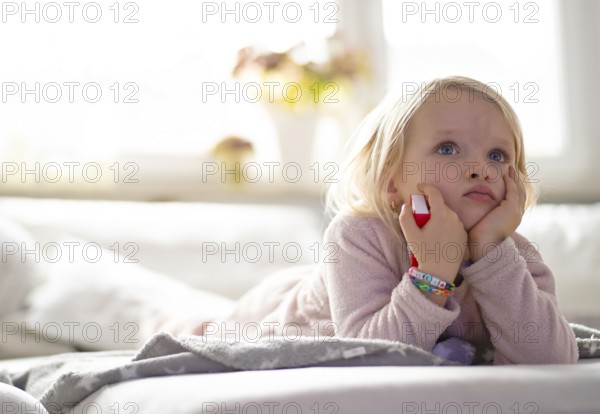 Child, girl, 4 years, blonde, lying on sofa, watching TV, watching television, watching television, excited, Stuttgart, Baden-Württemberg, Germany