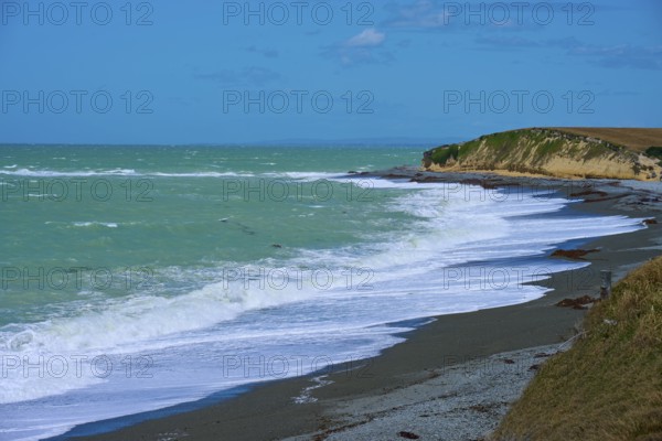 Waves crash against a rocky coast with blue sky, Tuhawaiki Point Lighthouse or Jack's Point Lighthouse, Scarborough, Timaru, South Island, New Zealand