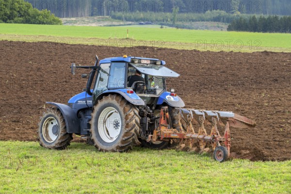 Tractor with plough, agricultural ploughing machine working on a field in autumn, fall in the Belgian Ardennes, Luxembourg, Wallonia, Belgium