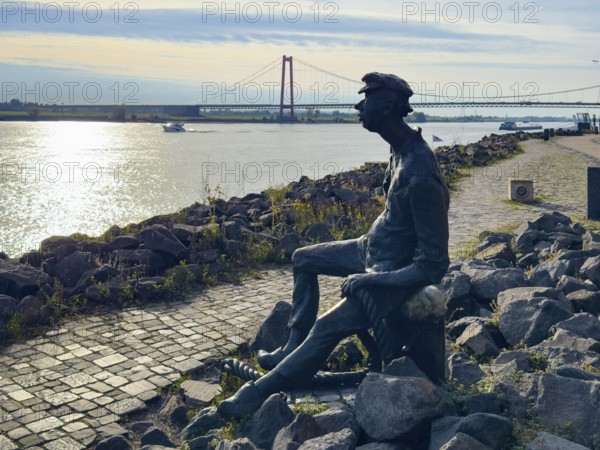 Photo with melancholy mood of bronze sculpture Poortekerl looking at Rhine waiting for ship to unload, Rhine navigation inland shipping, reminiscence of old times, bronze statue by artist Heide Friede-Kinalzik, Emmerich, Lower Rhine, North Rhine-Westphalia, Germany