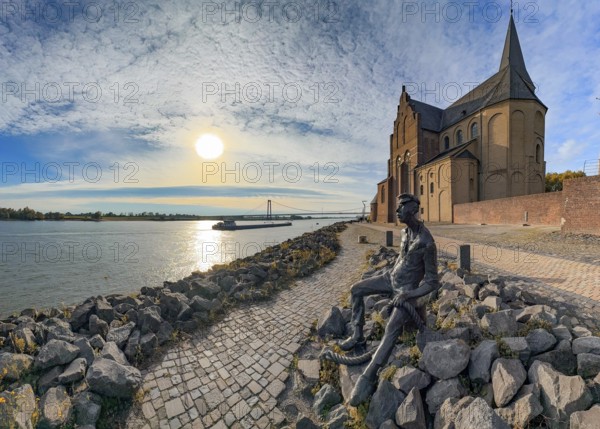 Photo with melancholy mood of bronze sculpture Poortekerl looking at Rhine waiting for ship to unload, Rhine navigation inland navigation, reminiscence of old times, bronze statue by artist Heide Friede-Kinalzik, rebuilt church of St. Martini destroyed in the Second World War, Emmerich, Lower Rhine, North Rhine-Westphalia, Germany
