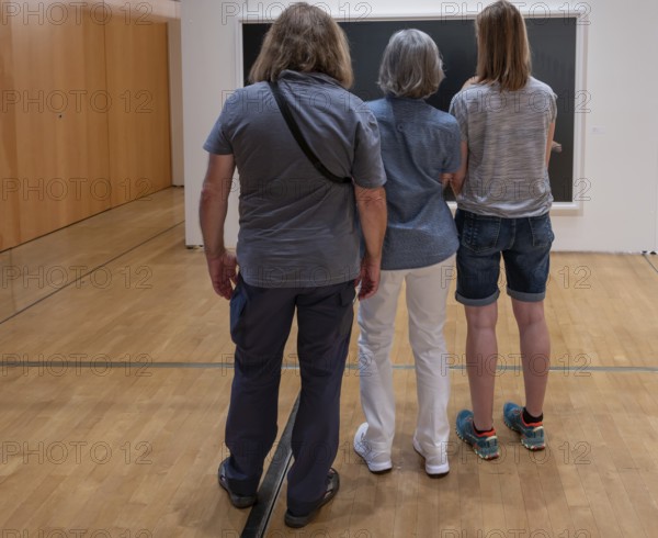 Three visitors look at a painting in an exhibition, Bavaria, Germany