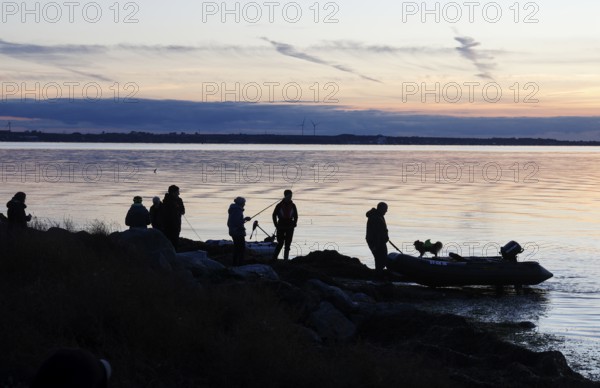 Angler on the beach during sunset, an angler docks on the shore with his inflatable boat and dog, Fehmarn island, 18.10.2025, Fehmarn, Schleswig-Holstein, Germany