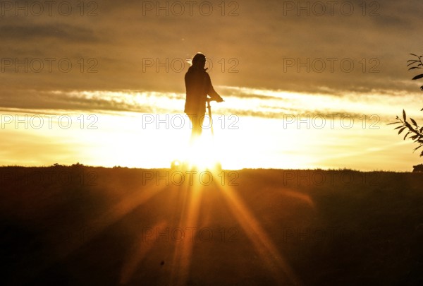 E-scooter drivers ride across a dike on the island of Fehmarn at sunset, 13.10.2025, Fehmarn, Schleswig-Holstein, Germany