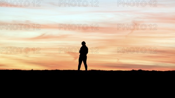 Woman with cell phone running on a dike at sunset, Fehmarn Island, 13.10.2025, Fehmarn, Schleswig-Holstein, Germany