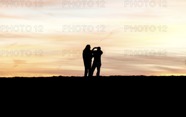 Walkers with mobile phone at sunset on a dike, Fehmarn island, 13.10.2025, Fehmarn, Schleswig-Holstein, Germany