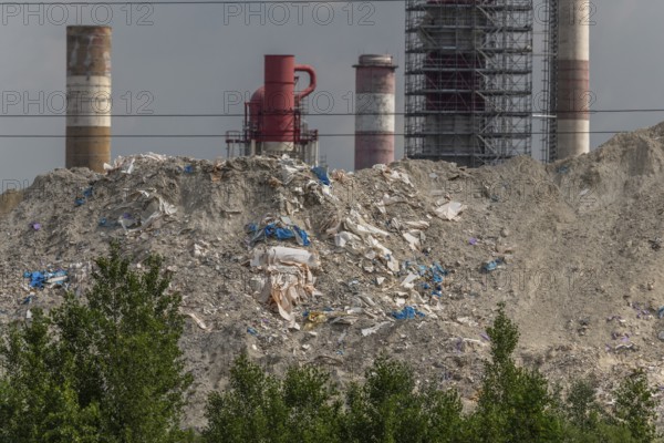 Chimneys, which are not far from factories, rise over mountains of waste. The sky is cloudy and creates a heavily polluted atmosphere. Haut Rhin, Alsace, France