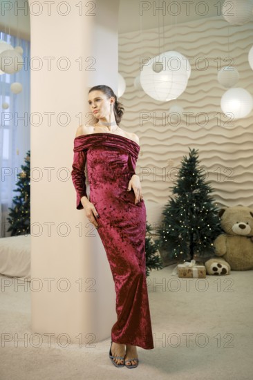A woman dressed in a stunning red velvet gown stands gracefully in a beautifully decorated room