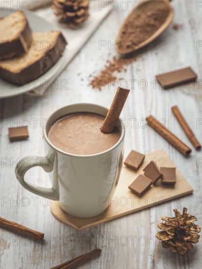 A cup of hot chocolate with cinnamon stick surrounded by cocoa powder and cake