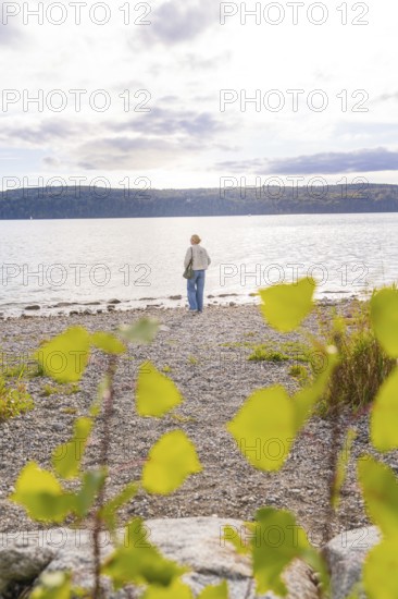 Person on a pebble beach looking at the lake on a cloudy day, Überlingen, Lake Constance, Germany