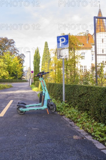 An electric scooter is parked on a sidewalk next to a parking sign against an autumn backdrop, Überlingen, Lake Constance, Germany
