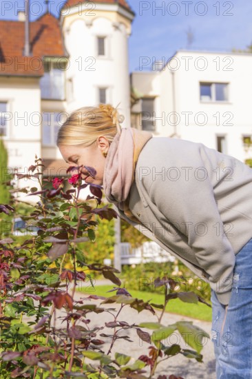 Woman with red hair enjoying the scent of flowers in autumn garden, Überlingen, Lake Constance, Germany