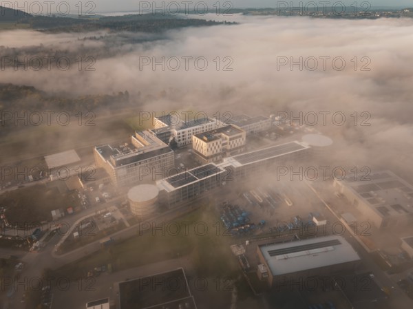 Building in an industrial area seen from above in fog, surrounded by landscape at daybreak, new hospital health campus building, Calw, Germany