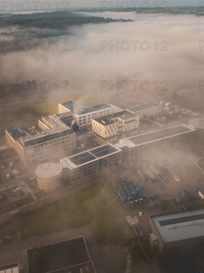 Aerial view of a complex of buildings in thick morning fog, modernly embedded in a natural landscape, new hospital health campus building, Calw, Germany