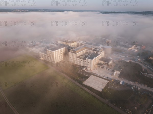 Industrial buildings seen from the air in morning fog, surrounded by natural landscape at dusk, new hospital health campus building, Calw, Germany