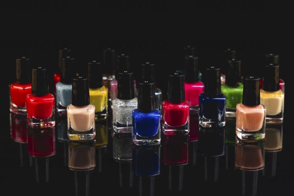 Different bottles of colored nail polishes with reflection on black background