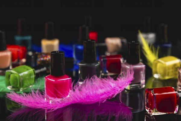 Colourful nail polish bottles and coloured feathers on black surface with reflection