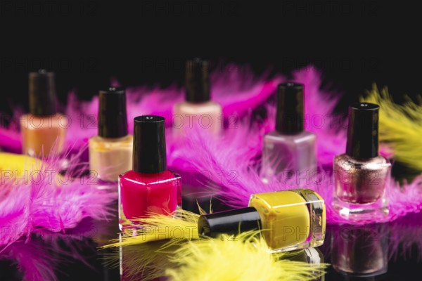 Pink and yellow nail polishes with feathers on black surface with reflection