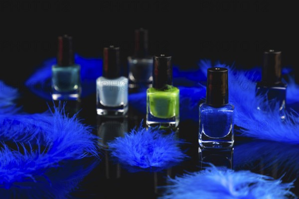 Nail polish bottles in shades of blue and green with blue feathers on a black surface with reflection