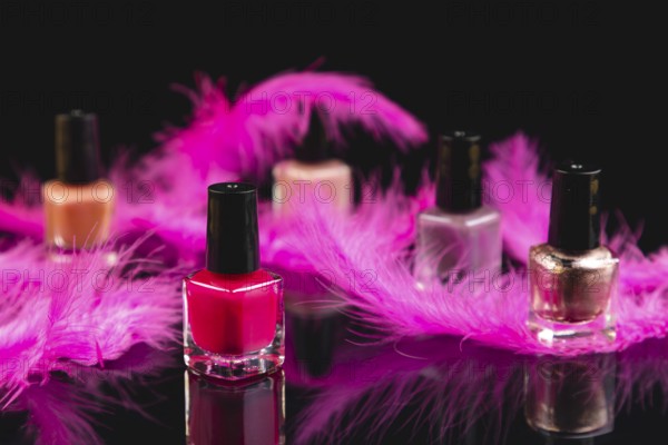 Pink and pink nail polishes with pink feathers on black surface with reflection