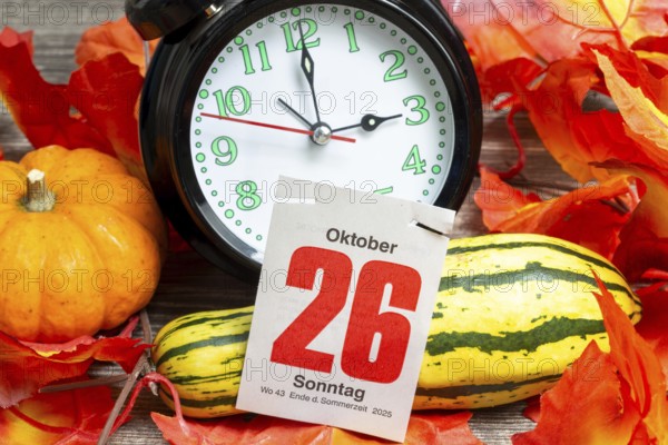 Time changeover to winter time 2025: Close-up of an alarm clock, autumnal decoration and a page from a tear-off calendar showing the date 26 October