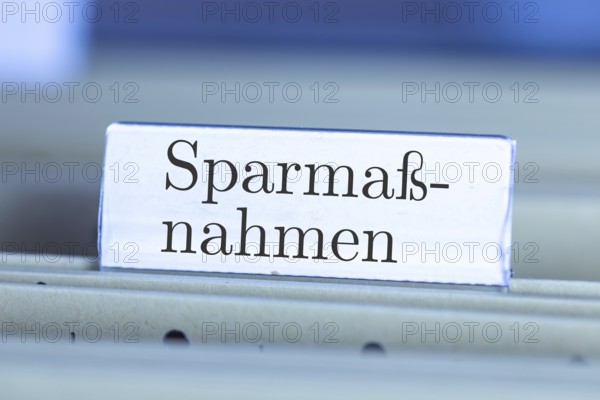 (Photomontage) Sign with the inscription SPARMASSNAHMEN on a suspension file folder