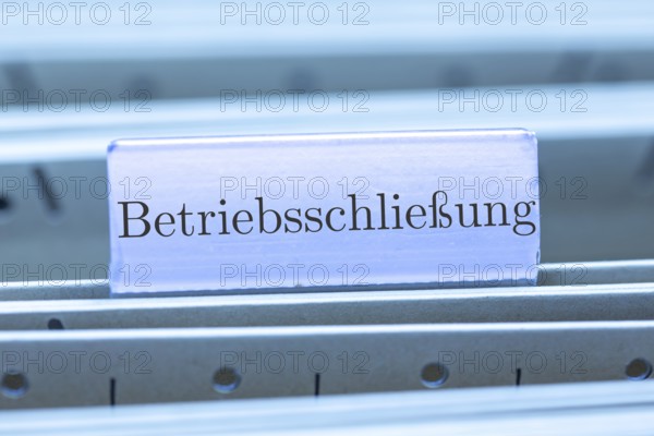 (Photomontage) Sign with the inscription BETRIEBSSCHLIESSUNG on a suspension file index