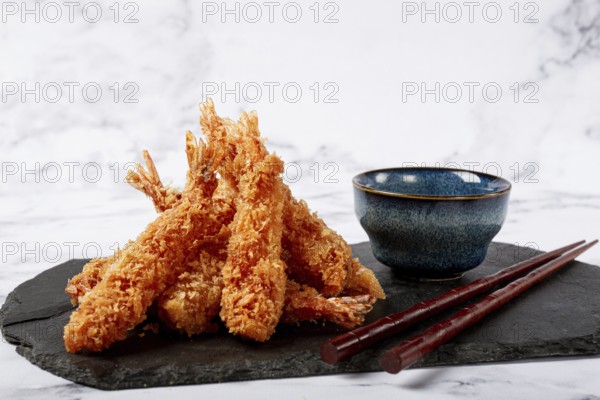 Shrimp in tempura, deep fried, on black slate, with sauce, light marble table, no people