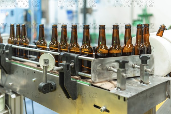 Empty glass beer bottles traveling on a stainless steel conveyor belt within a modern brewing factory, representing industrial production and automated bottling processes