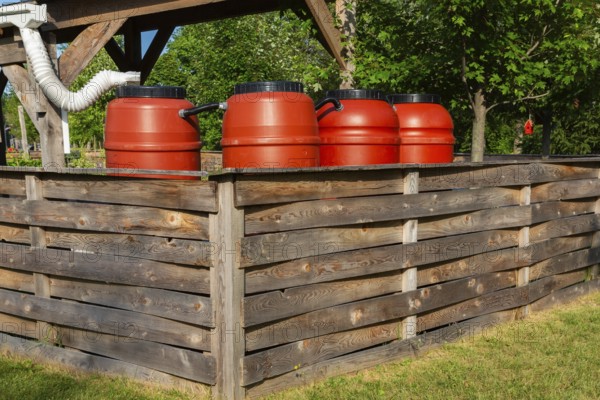 Reddish brown plastic water butts collecting and storing rain water from white plastic downspout in community garden enclosure in summer, Quebec, Canada