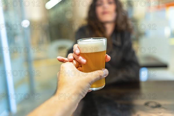 Hand holding a refreshing glass of craft beer, presenting it to a woman in a bar, representing tasting, brewery visits, social gatherings, and enjoying drinks