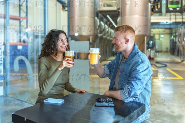 Two friends clinking glasses of craft beer during a tasting at a modern industrial brewery, smiling and enjoying a relaxed, social weekend experience indoors