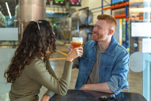 Young couple on a brewery date tasting craft beer, smiling and relaxed in a modern industrial taproom, enjoying pints, conversation and a cheerful weekend outing