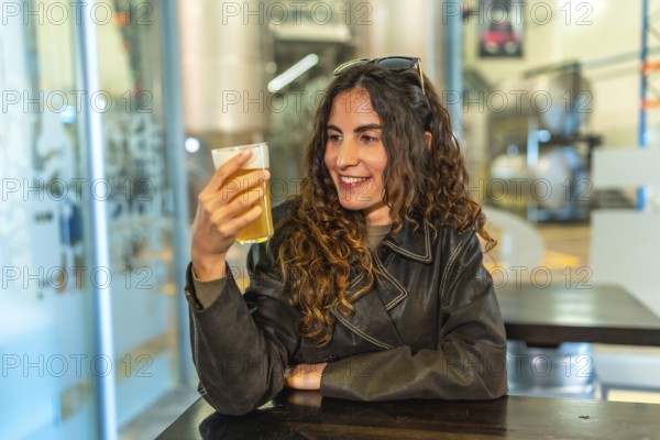 Woman in a leather jacket smiling and savoring a glass of craft beer at a modern brewery bar, enjoying a relaxed tasting experience with friends in a casual weekend hangout