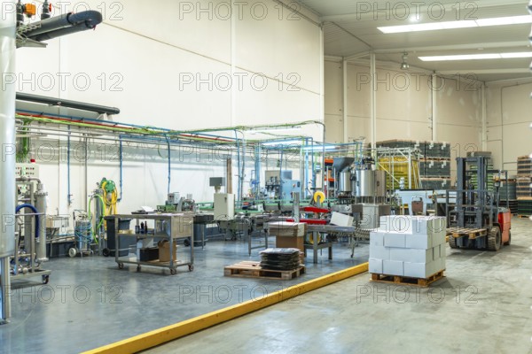 Industrial brewery interior featuring automated production lines, bottling machinery, tanks, pipes, and a forklift stacking goods, illustrating the process of beverage manufacturing