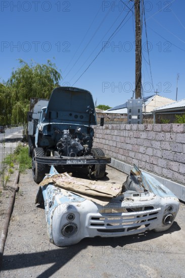 A dismantled old lorry with visible engine in front of a wall under a blue sky, engine repair, Armenia