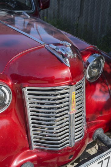 Front of a shiny red vintage car with a striking emblem in the sun, Moskvich 401, Armavir province, Armenia