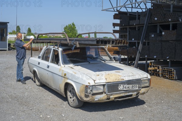 A rusty old car with a man putting metal rods on it, middle class car GAZ-24 Volga, Norapat, Armavir province, Armenia