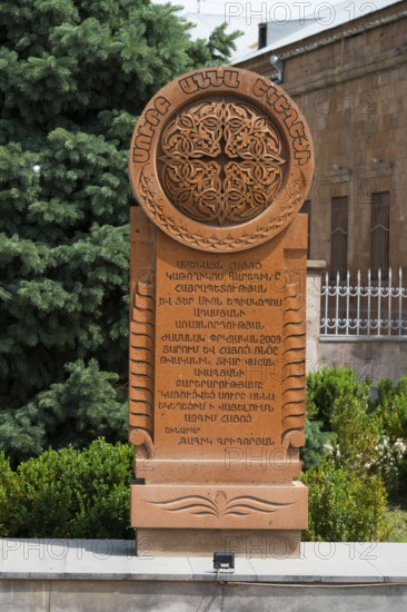 An elaborately engraved stone khachkar with complex ornaments and Armenian characters, surrounded by trees and plants, Khachkar, cross stone, Aghavnatun, Armavir province, Armenia