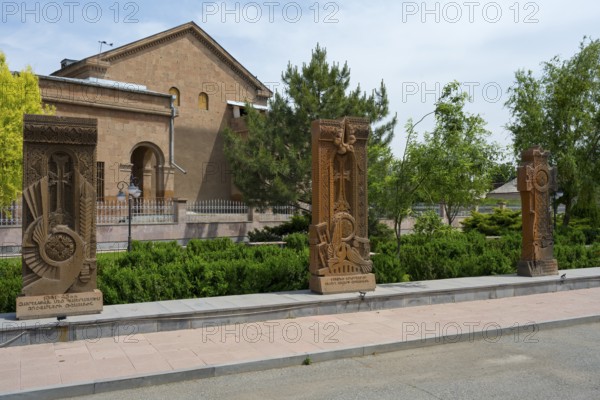 Three ornately decorated khachkars in front of a historic building, surrounded by green trees and well-tended hedges, Khachkar, Cross Stone, Aghavnatun, Armavir Province, Armenia