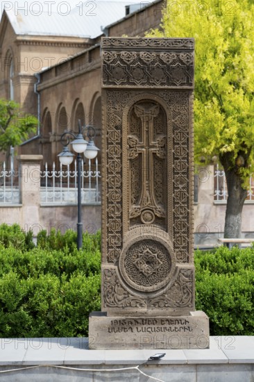 A detailed khachkar with a cross motif and rich ornamentation in front of a church façade, surrounded by trees, Khachkar, cross stone, Aghavnatun, Armavir Province, Armenia