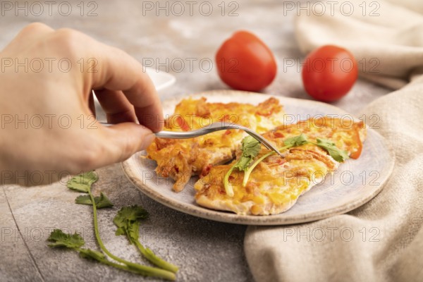 Baked chicken meat with cheese and tomatoes with hand on brown concrete background and linen textile. side view, close up, selective focus