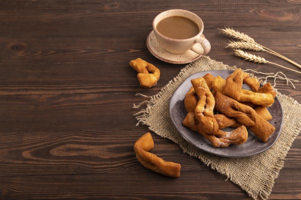 Crunchy biscuit Brushwood cookies sprinkled with powdered sugar on brown wooden background and linen textile, cup of coffee, side view, copy space
