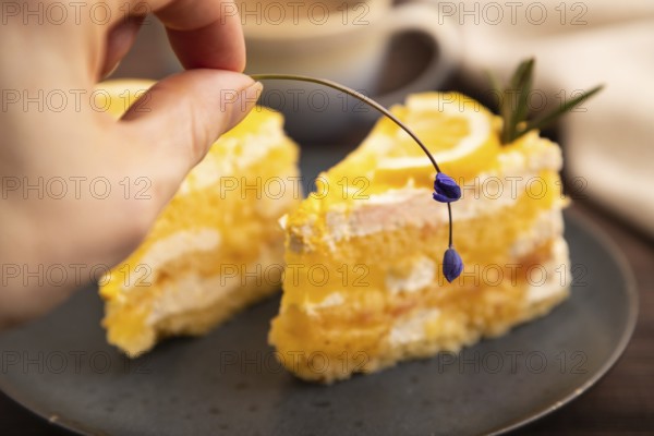 Lemon cake with hand on brown wooden background and linen textile, cup of coffee, side view, close up, selective focus