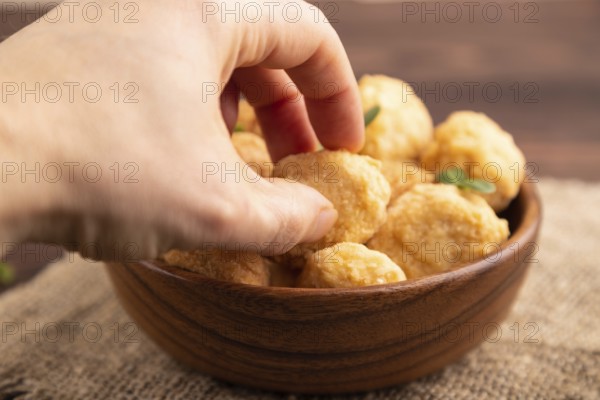 Fried crispy Chicken Nuggets with ketchup, microgreen on brown wooden background and linen textile with hand. side view, close up, selective focus