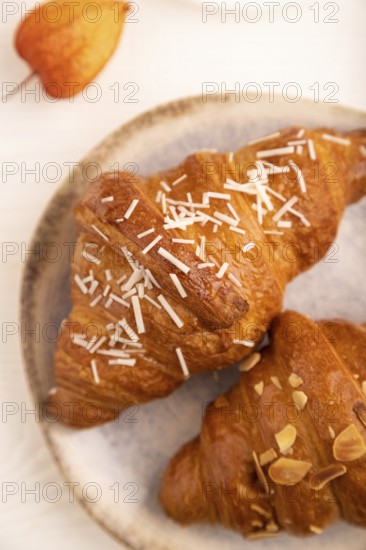 Croissant on blue plate on white wooden background and orange linen textile, cup of coffee, side view, close up, selective focus